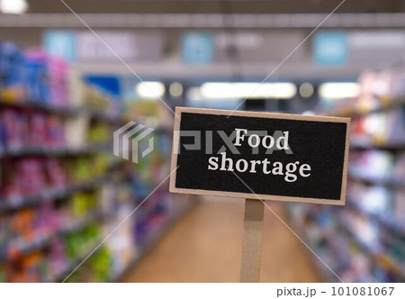 Wooden information label sign with text FOOD SHORTAGE against defocused store shelves message. Global hunger, inflation, high prices, increasing living expenses and poverty, financial crisis, food 101081067