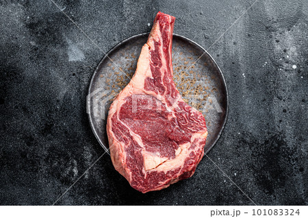 Raw cowboy steak, rib eye steak with bone, beef marbled meat on butcher cutting board. Black background. Top view. Copy space Raw cowboy steak, rib eye steak with bone, beef marbled meat on butcher cutting board. Black background. Top view. Copy space 101083324