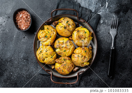 Broken potatoes baked in oil with herbs. Black background. Top view 101083335