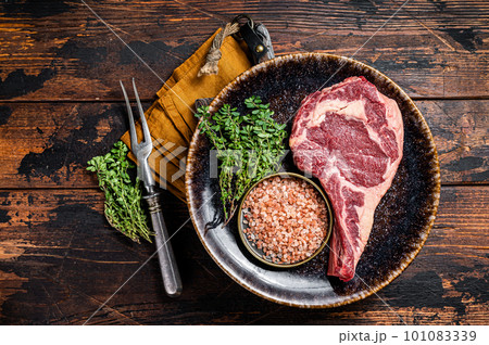 Raw prime cowboy or rib eye steak, dry aged beef meat. Wooden background. Top view Raw prime cowboy or rib eye steak, dry aged beef meat. Wooden background. Top view 101083339