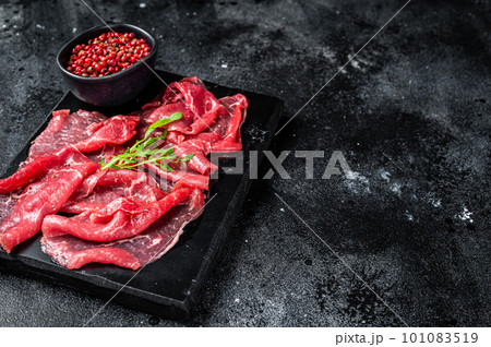 Slices of Beef Capriccio, raw marbled meat. Black background. Top view. Copy space Slices of Beef Capriccio, raw marbled meat. Black background. Top view. Copy space 101083519