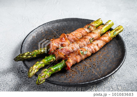 Plate with pork bacon wrapped asparagus on grey table. White background. Top view 101083683