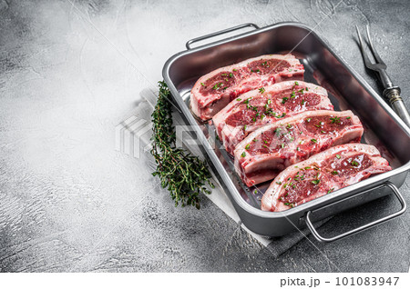Marinated Raw meat of lamb mutton saddle in steel tray with thyme, spices and olive oil. White background. Top view. Copy space Marinated Raw meat of lamb mutton saddle in steel tray with thyme, spices and olive oil. White background. Top view. Copy space 101083947