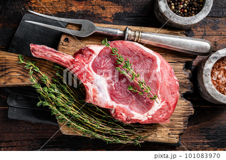 Uncooked Raw Rib eye or Tomahawk beef (veal) steak on butcher cutting board. Wooden background. Top view 101083970