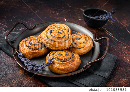 Sweet twisted Bun with poppy seeds and lavender. Dark background. Top view Sweet twisted Bun with poppy seeds and lavender. Dark background. Top view 101083981