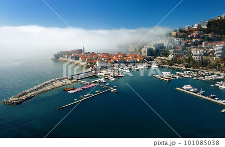 Mysterious drone view of the ancient city of Budva during heavy cloud cover. Old medieval city with red roofs in Montenegro on the sunset. Mysterious drone view of the ancient city of Budva during heavy cloud cover. Old medieval city with red roofs in Montenegro on the sunset. 101085038