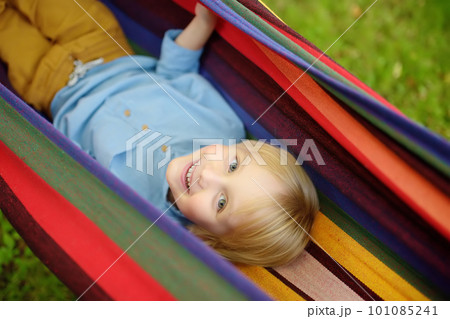 Cute little blond white boy enjoy and having fun with multicolored hammock in backyard or outdoor playground. Summer outdoors active leisure for kids. Child Cute little blond white boy enjoy and having fun with multicolored hammock in backyard or outdoor playground. Summer outdoors active leisure for kids. Child 101085241