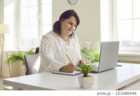 Overweight brunette young woman using laptop in modern office Overweight brunette young woman using laptop in modern office 101086946