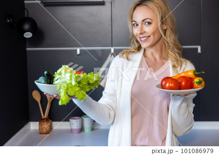 Cheerful young housewife showing salad ingredients before the camera Cheerful young housewife showing salad ingredients before the camera 101086979