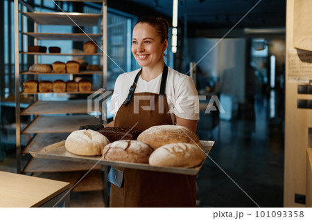 Pretty woman baker holding variety of baked bread on tray Pretty woman baker holding variety of baked bread on tray 101093358
