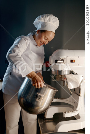 Female baker working in professional kitchen with dough mixer at bakery 101093397