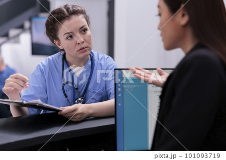 Medical assistant showing patient expertise to receptionist while asking her to programming another examination. Medical staff working in hospital waiting area, health care service support Medical assistant showing patient expertise to receptionist while asking her to programming another examination. Medical staff working in hospital waiting area, health care service support 101093719