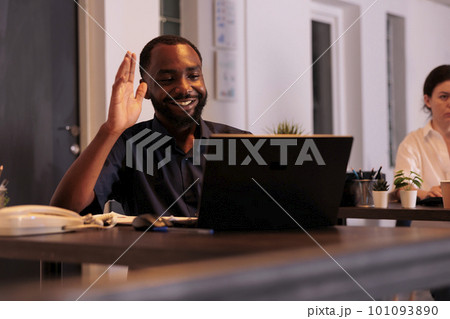 Smiling employee talking on videoconference with teamlead, waving hi, corporate worker answering teleconference call in office at night. African american man remote conversation in coworking space Smiling employee talking on videoconference with teamlead, waving hi, corporate worker answering teleconference call in office at night. African american man remote conversation in coworking space 101093890