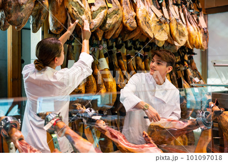 Young couple work together in butcher shop - they cut traditional Spanish jamon Young couple work together in butcher shop - they cut traditional Spanish jamon 101097018