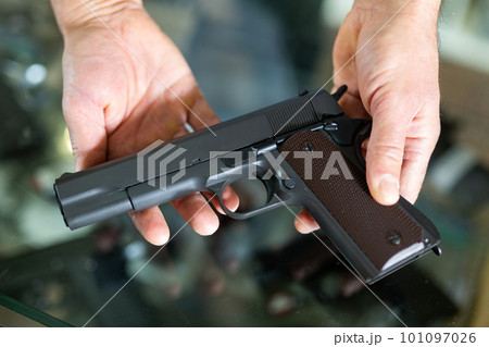Gunsmith shop assistant demonstrates black pistol in hands 101097026