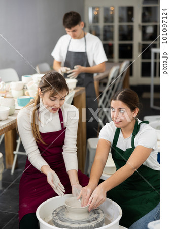 Two young women sculpt product on potter's wheel Two young women sculpt product on potter's wheel 101097124