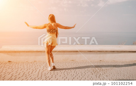 Woman summer dance. Silhouette of a happy woman who dances, spins and raises her hands to the sky. A playful young woman enjoys her happy moment dancing in the rays of the golden sun. 101102254