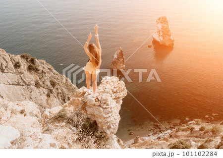Woman travel sea. Happy tourist enjoy taking picture outdoors for memories. Woman traveler looks at the edge of the cliff on the sea bay of mountains, sharing travel adventure journey 101102284