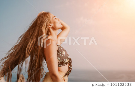 Woman travel sea. Happy tourist taking picture outdoors for memories. Woman traveler looks at the edge of the cliff on the sea bay of mountains, sharing travel adventure journey 101102338