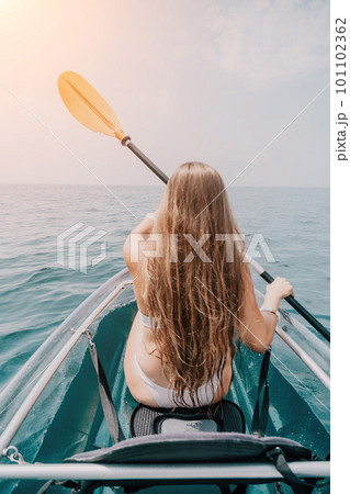 Woman in kayak back view. Happy young woman with long hair floating in transparent kayak on the crystal clear sea. Summer holiday vacation and cheerful female people relaxing having fun on the boat Woman in kayak back view. Happy young woman with long hair floating in transparent kayak on the crystal clear sea. Summer holiday vacation and cheerful female people relaxing having fun on the boat 101102362