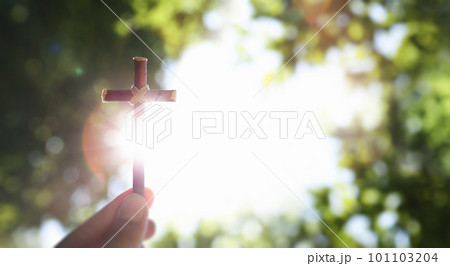 Fresh morning blue sky and green lush tree forest background and bright sun shining through the cross of Jesus Christ in hand Fresh morning blue sky and green lush tree forest background and bright sun shining through the cross of Jesus Christ in hand 101103204