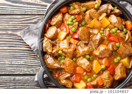 Slow cooked beef with potatoes, carrots, tomatoes, green peas, onions and spices close-up on a wooden table. Horizontal top view 101104837