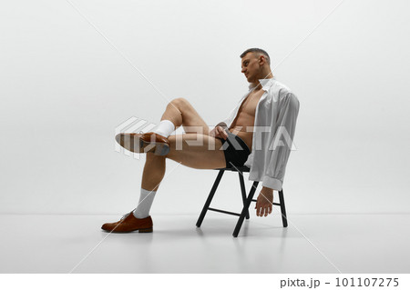 One attractive man sitting on chair with unbuttoned shirt and looking away over white studio background One attractive man sitting on chair with unbuttoned shirt and looking away over white studio background 101107275