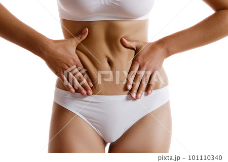 Young body of girl in white underwear, showing fat on her belly, posing isolated on white. Plastic surgery, aesthetic cosmetology concept. Close-up. Young body of girl in white underwear, showing fat on her belly, posing isolated on white. Plastic surgery, aesthetic cosmetology concept. Close-up. 101110340