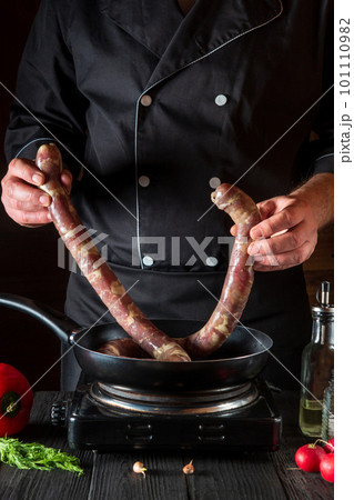The cook puts raw meat sausage into the pan before cooking. Working environment in restaurant kitchen with vegetables and spices on the table The cook puts raw meat sausage into the pan before cooking. Working environment in restaurant kitchen with vegetables and spices on the table 101110982