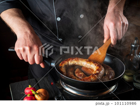 Cooking meat sausage in the restaurant kitchen. The chef fries sausage in frying pan. The idea of a delicious meat dish Cooking meat sausage in the restaurant kitchen. The chef fries sausage in frying pan. The idea of a delicious meat dish 101110986