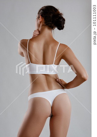 Perfect, young body of a girl in white underwear posing back against grey background. Plastic surgery and aesthetic cosmetology concept. Close-up. Perfect, young body of a girl in white underwear posing back against grey background. Plastic surgery and aesthetic cosmetology concept. Close-up. 101111003