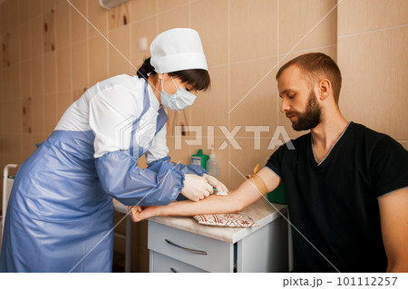 Doctor woman in a white robe makes an injection to a young man in the treatment room of the hospital. Doctor woman in a white robe makes an injection to a young man in the treatment room of the hospital. 101112257