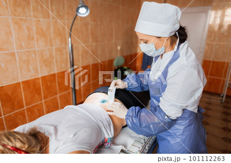 Nurse lubricates the wound with an antibacterial solution after surgery and applies bandages to the wound to a young woman in a hospital ward. Providing patient care Nurse lubricates the wound with an antibacterial solution after surgery and applies bandages to the wound to a young woman in a hospital ward. Providing patient care 101112263