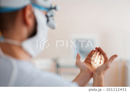 Doctor neurosurgeon in a medical mask in professional magnifying glasses shines on the hands checks binocular loupes. Preparation in the operation. Back view 101112431