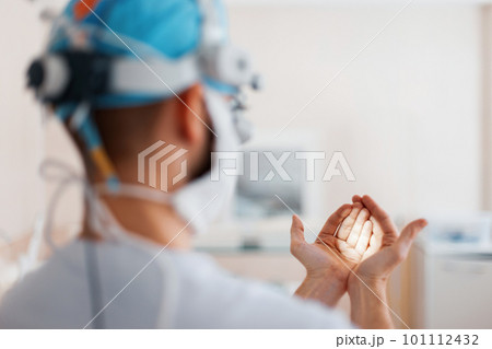 Doctor surgeon in medical mask in professional magnifying glasses shines on his hand with a flashlight, preparing for surgery. Back view 101112432