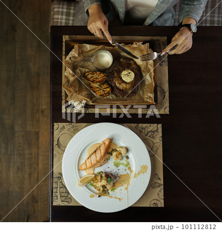 Woman with a knife and fork cuts a meat steak with vegetables in a restaurant. Lunch break. The concept of a healthy dinner. Top view of the dining table 101112812