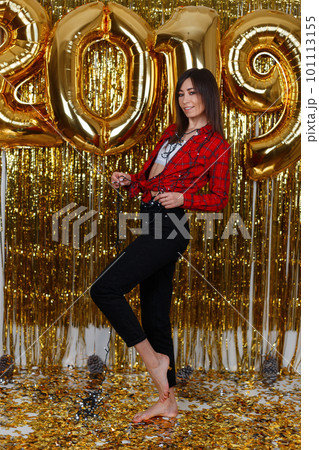 Beautiful happy woman in stylish clothes posing at a party against the background of golden balloons 2019. Girl is having fun and enjoying the holiday. The concept of celebrating Christmas 101113155