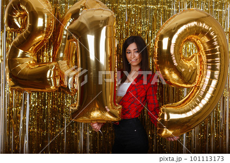 Young happy woman in shirt in jeans posing with balloons of golden color 2019 on the background of shiny Christmas garlands. Merry Christmas. Beautiful girl celebrates New Year. Young happy woman in shirt in jeans posing with balloons of golden color 2019 on the background of shiny Christmas garlands. Merry Christmas. Beautiful girl celebrates New Year. 101113173