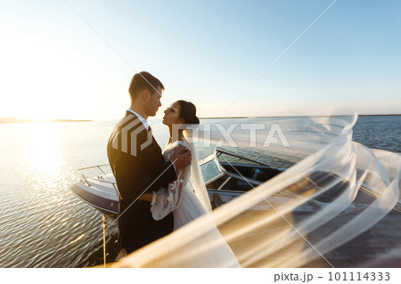 Pretty bride and stylish groom together on the bridge against the background of the boat. Together. Wedding. 101114333