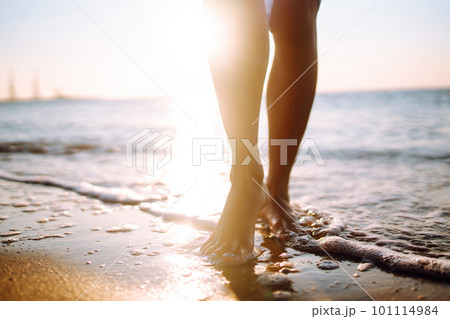 Close- up leg of young woman walking along wave of sea water and sand on the summer beach. 101114984
