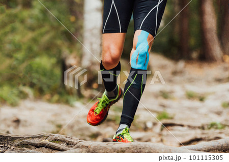 legs male runner with kinesio tape on knee running forest 101115305