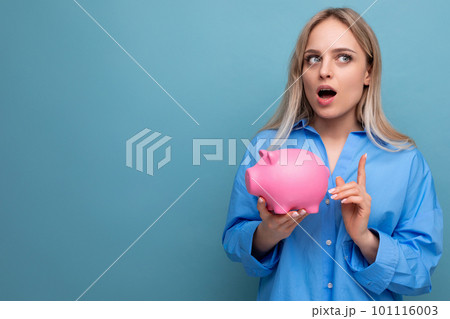 pensive blond girl holding a piggy bank with a stock thinks where to spend money on a blue isolated pensive blond girl holding a piggy bank with a stock thinks where to spend money on a blue isolated 101116003