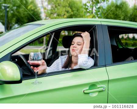Beautiful young modern girl driving a car with a glass of red wine in her hand. The female driver is alone in the car, drinking wine. Drunken stalker. Violation of traffic rules Beautiful young modern girl driving a car with a glass of red wine in her hand. The female driver is alone in the car, drinking wine. Drunken stalker. Violation of traffic rules 101116828