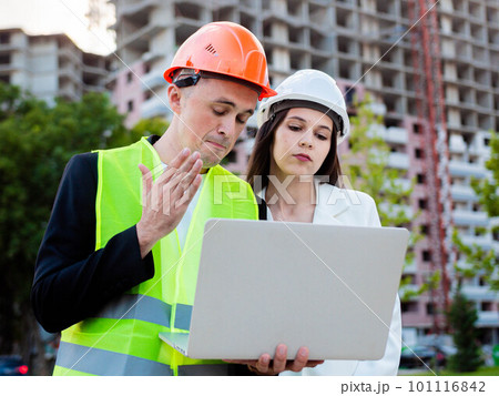 Young male builder and female engineer explain and check the construction and repair of a multi-storey building. House on construction site, outdoors. Young male builder and female engineer explain and check the construction and repair of a multi-storey building. House on construction site, outdoors. 101116842