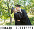 Graduates in robes stand in a university whipping and kiss 101116861
