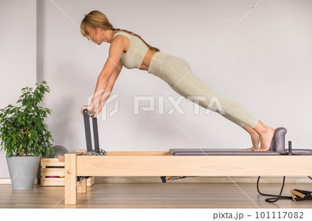 Woman training pilates on the reformer bed. - Stock Photo