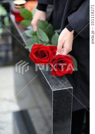 Woman with red roses near black granite tombstone outdoors, closeup. Funeral ceremony 101118271