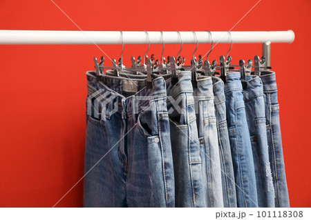 Rack with stylish jeans on red background, closeup Rack with stylish jeans on red background, closeup 101118308