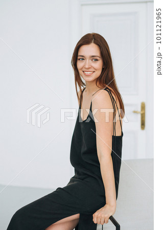 Young woman with long hair on evening elegant black dress with open back in the white interior Young woman with long hair on evening elegant black dress with open back in the white interior 101121965