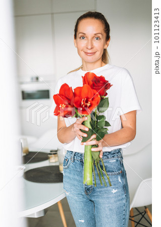 Young woman with bouquet of red flowers in hands near window in bright kitchen at home Young woman with bouquet of red flowers in hands near window in bright kitchen at home 101123413